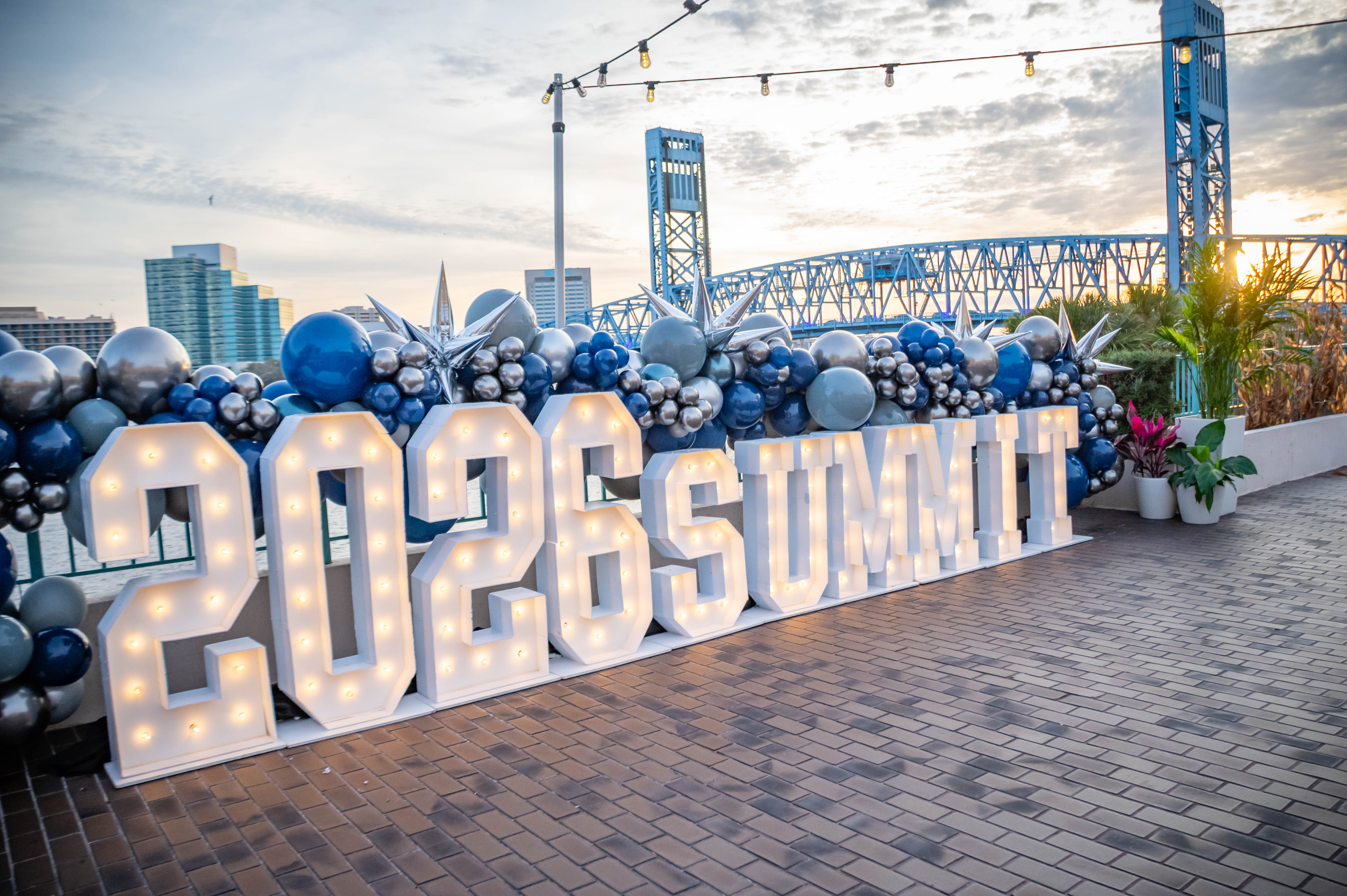Gray and blue balloons frame free-standing letters spelling "2026 Summit"