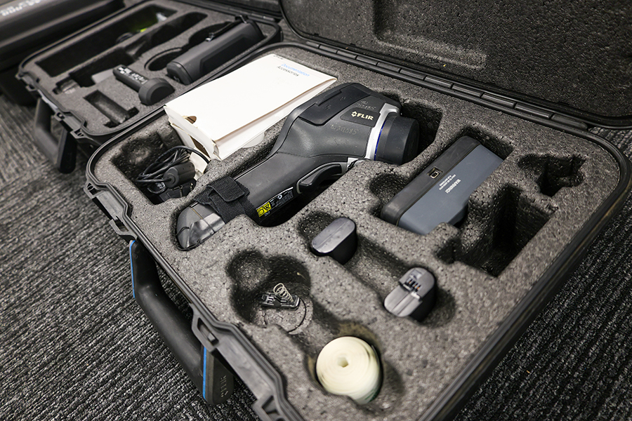 Infrared thermal camera kit with handheld scanner, batteries, charger, and accessories organized in a protective carrying case.